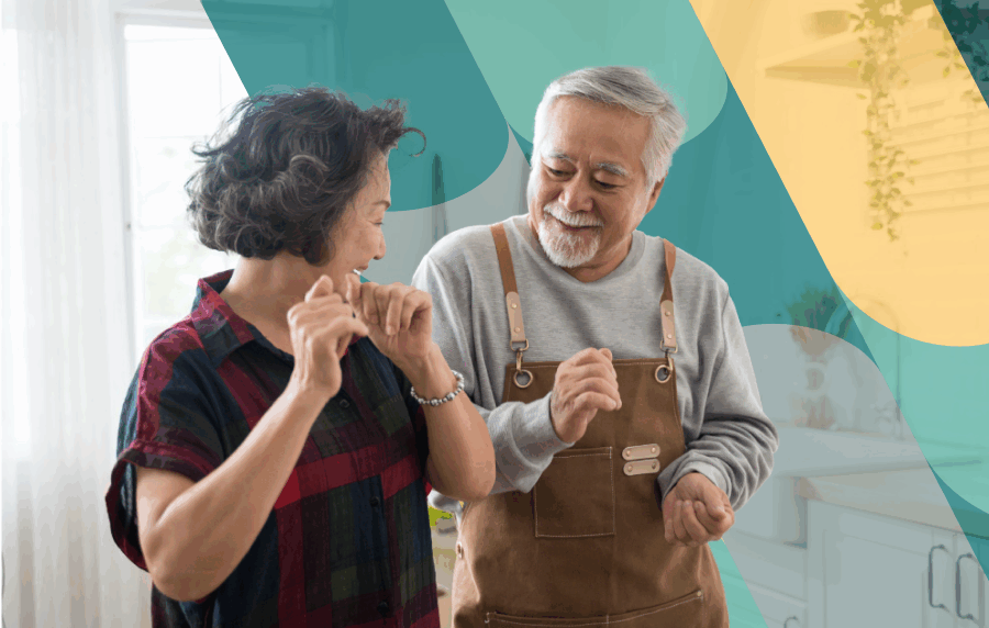 East Asian senior couple dancing in their home and smiling at one another