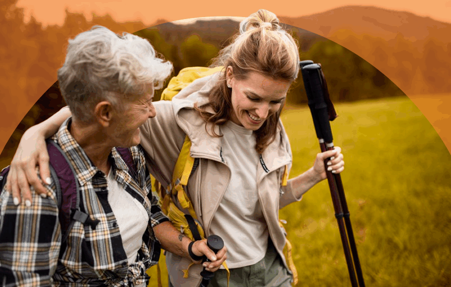 Young white woman with her arm around a sernior white woman, both holding hiking poles and walking outside