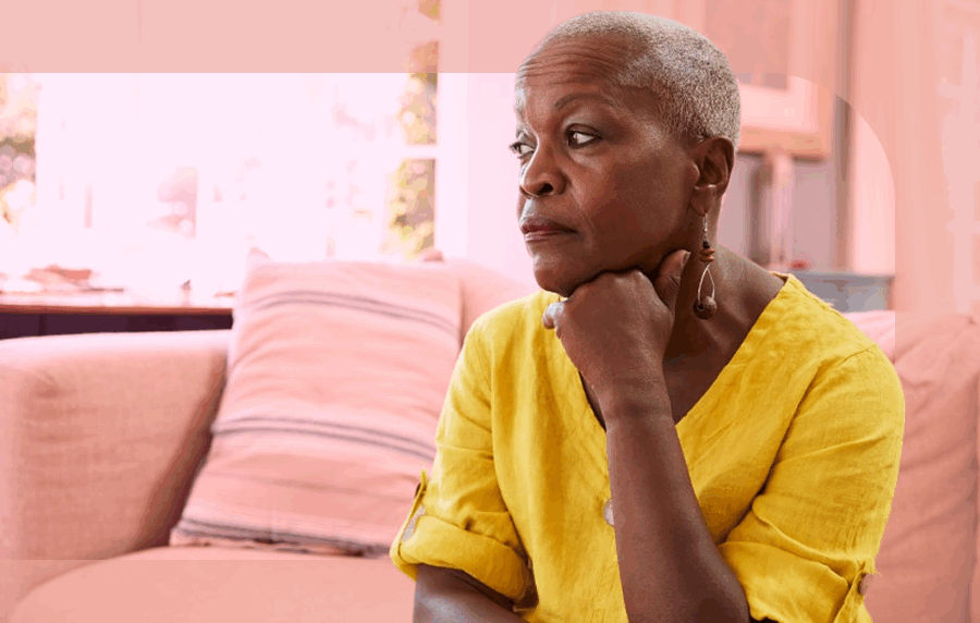 Middle-aged or senior Black woman in yellow shirt sitting on a couch with a somber expression