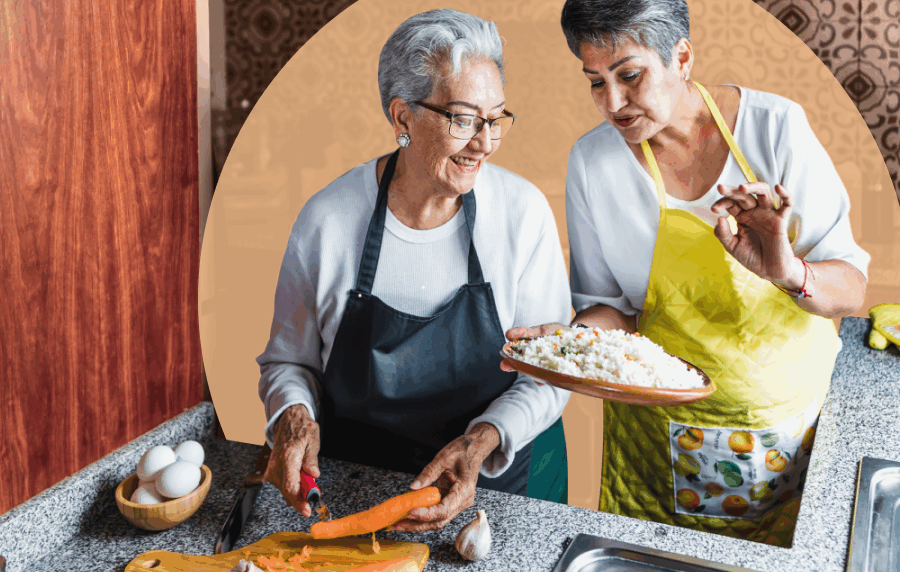 Two senior Hispanic women wearing aprons and chopping vegetables together in a kitchen