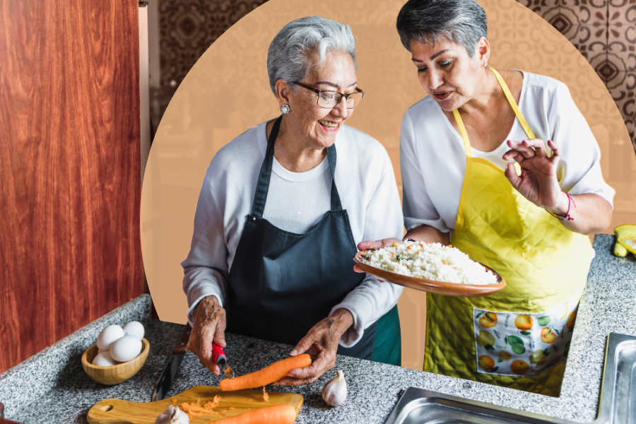 Two senior Hispanic women wearing aprons and chopping vegetables together in a kitchen