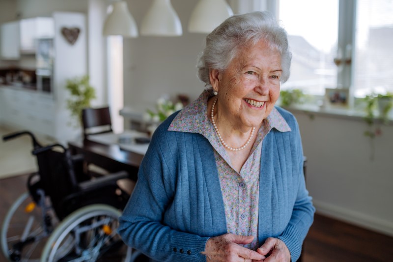 Portrait of smiling senior woman at home with her wheelchair in the background