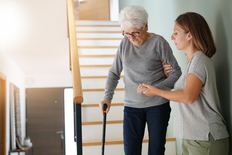 Female home caregiver helping elderly woman going down the stairs