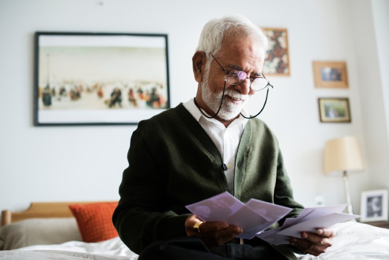 An elderly Indian man sitting on his bed looking at old photos and smiling