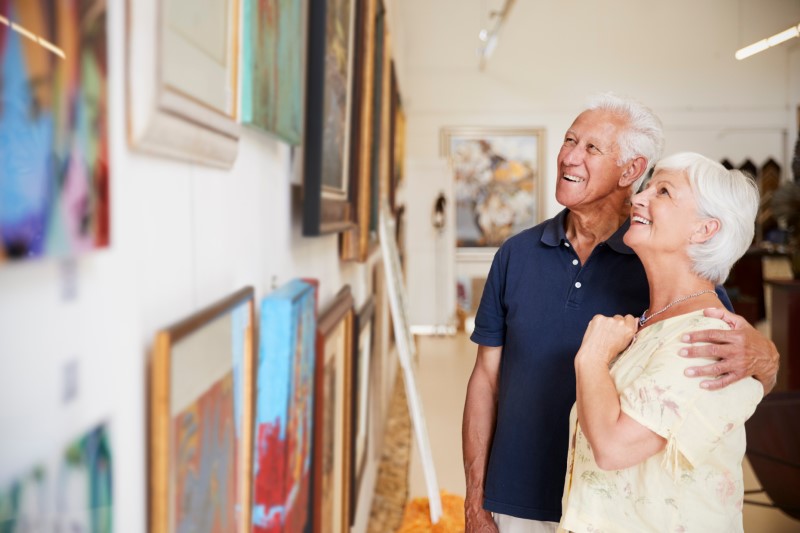 Senior Couple Looking At Paintings In Art Gallery while smiling