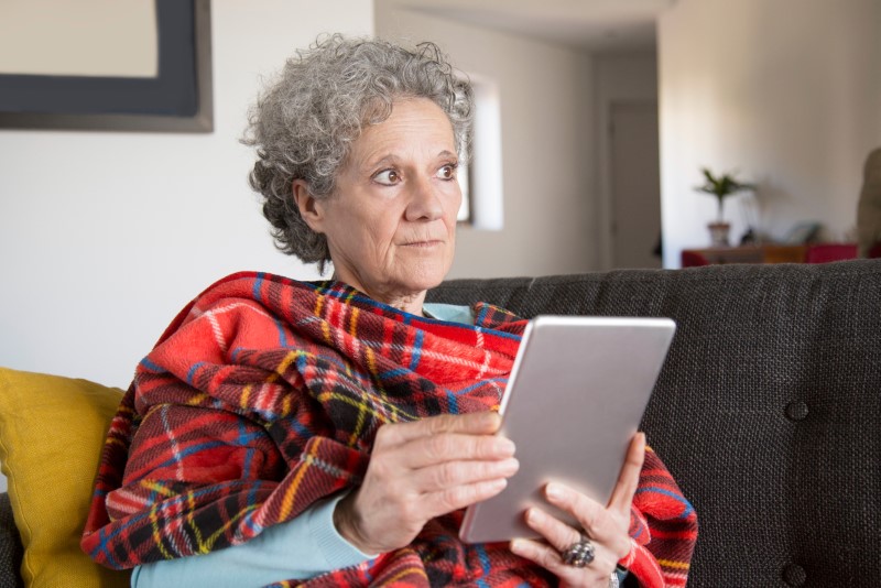 Pensive senior woman reading online book on tablet at home.