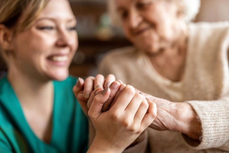 Senior woman holding the hands of a younger female caregiver with both smiling