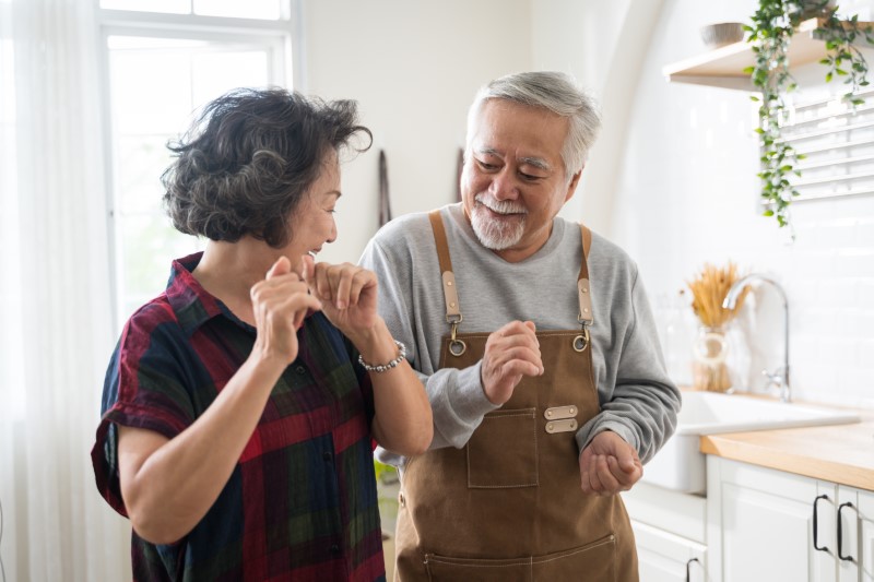 Senior Asian couple is dancing and smiling in kitchen at home.