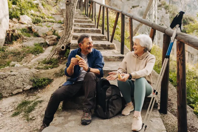 Senior couple having some bananas while sitting at the bottom of a hiking trail.