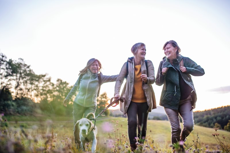 Senior women friends with dog on walk outdoors in nature