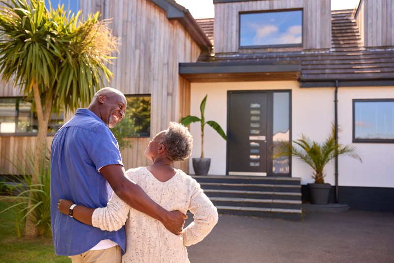 Rear View Of Senior Couple Standing In Driveway In Front Of Dream Home Together
