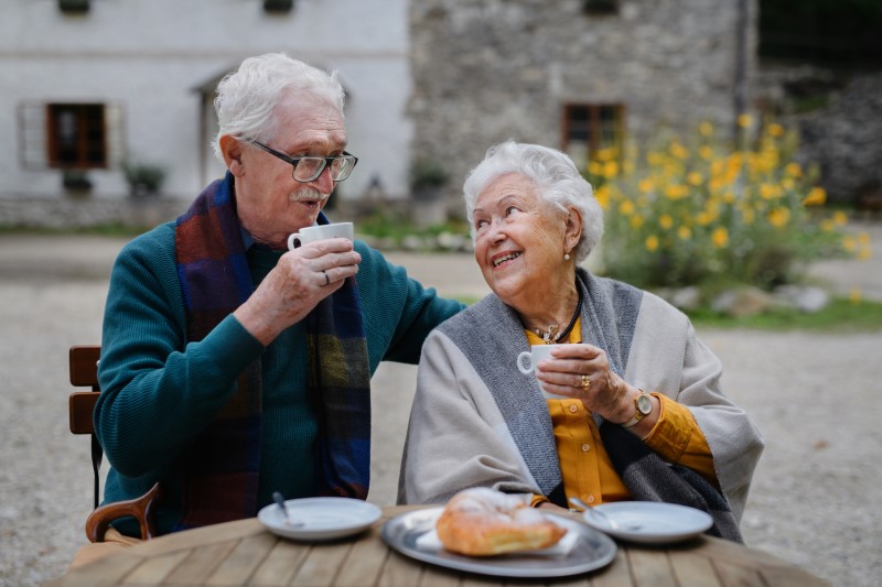Senior couple enjoying cup of coffee and croissant outdoor in a cafe.