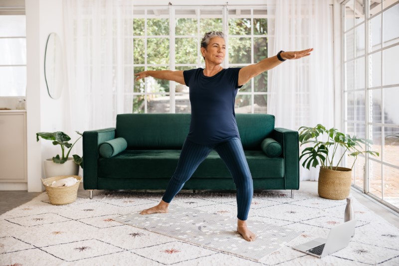 Active senior woman doing yoga in her living room, showing her strength and flexibility as she practices the powerful warrior pose.