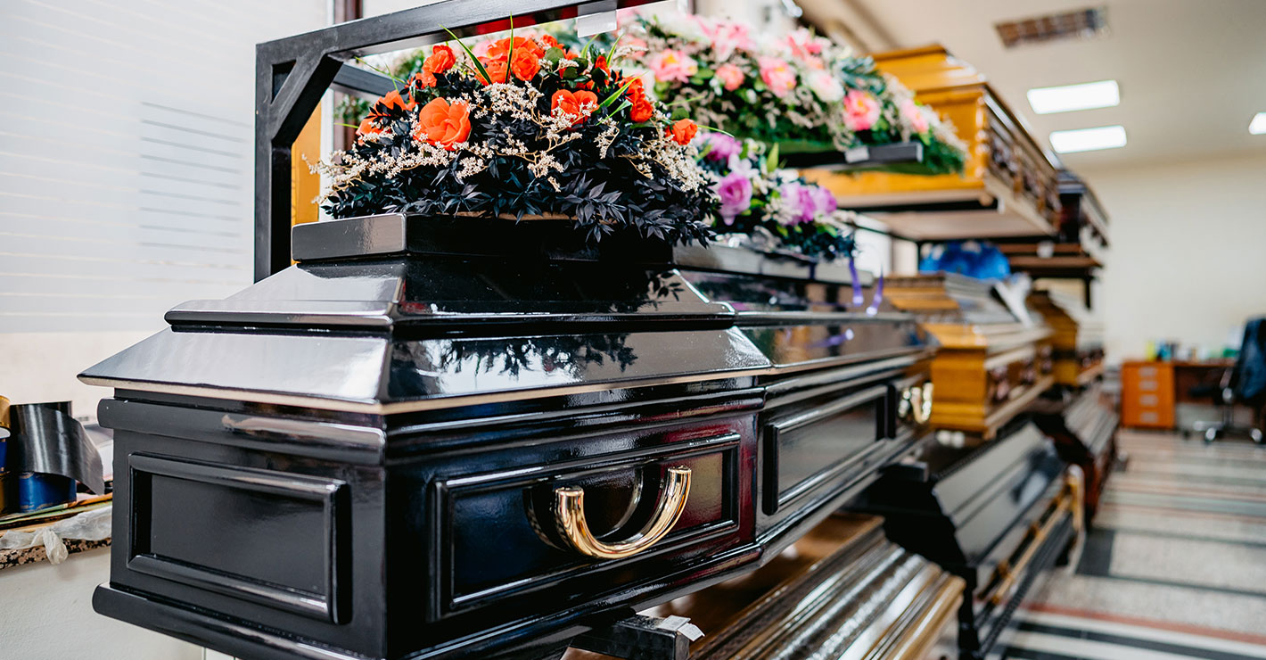 A black casket in a showroom has an arrangement of red roses on top. 