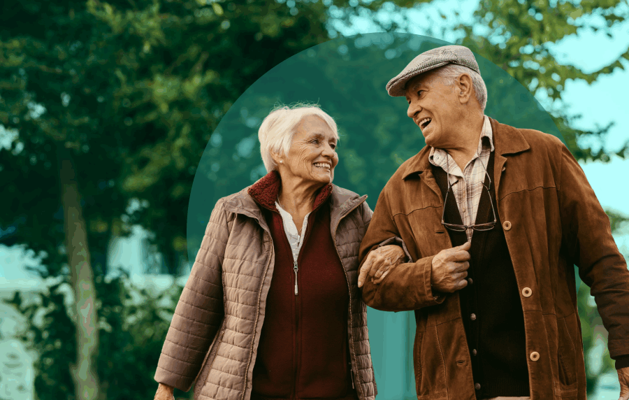 White senior couple wearing brown coats and walking outside, smiling at one another