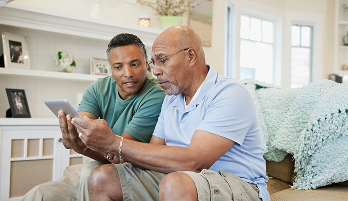 A man and his adult son look over insurance policy details on a tablet.