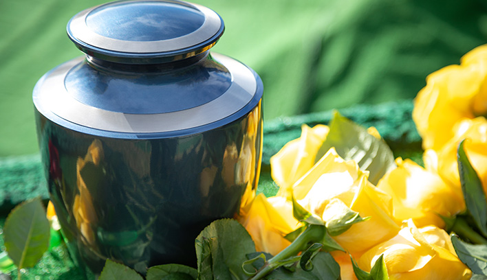 Closeup of a black, ceramic urn among yellow roses and greenery.