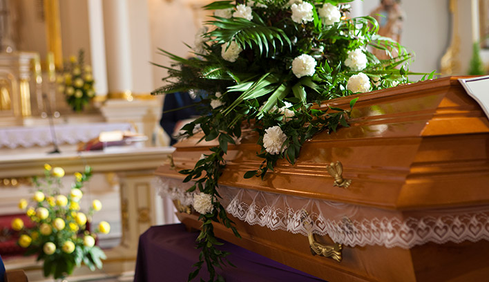 Close-up of a brown casket in a church with flowers.