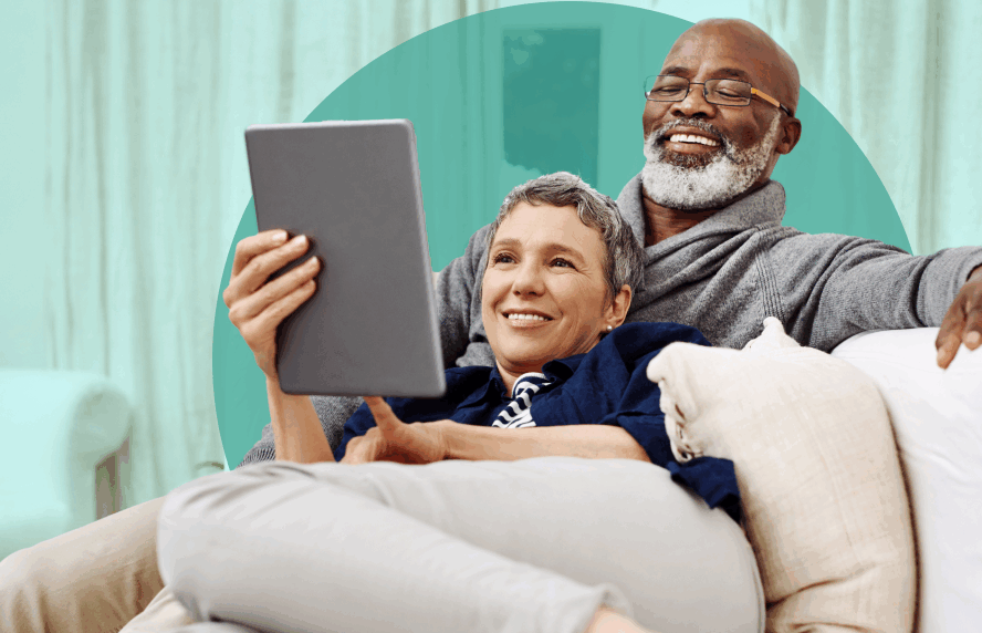 Smiling couple in their 60s on the couch together reading from a tablet screen