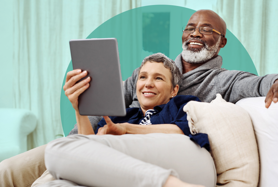 Smiling couple in their 60s on the couch together reading from a tablet screen