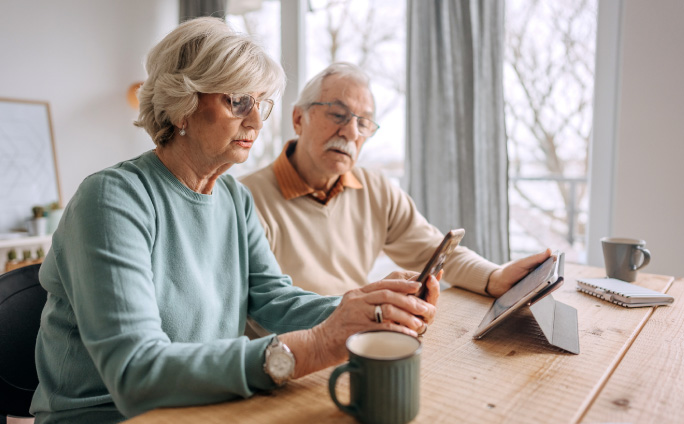A seated couple looks at their digital devices while funeral planning