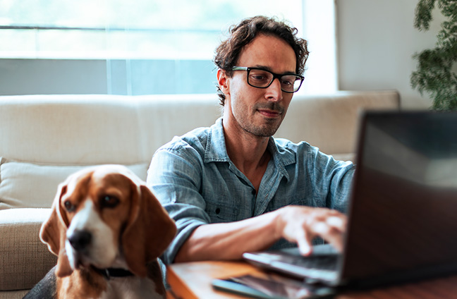 Man searches about life insurance questions on his laptop, while sitting at his coffee table with dog next to him