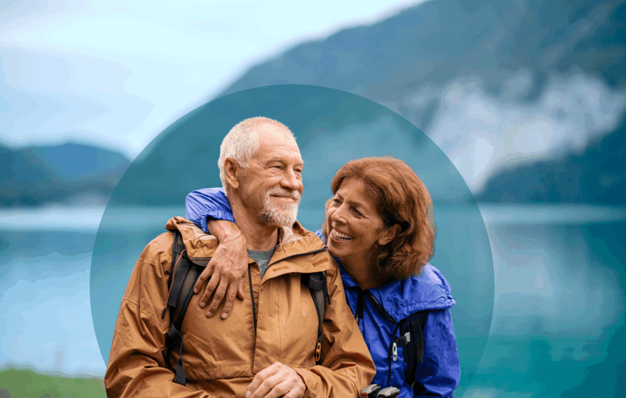 Smiling senior couple in wind breakers outside with a mountain and lake in the background