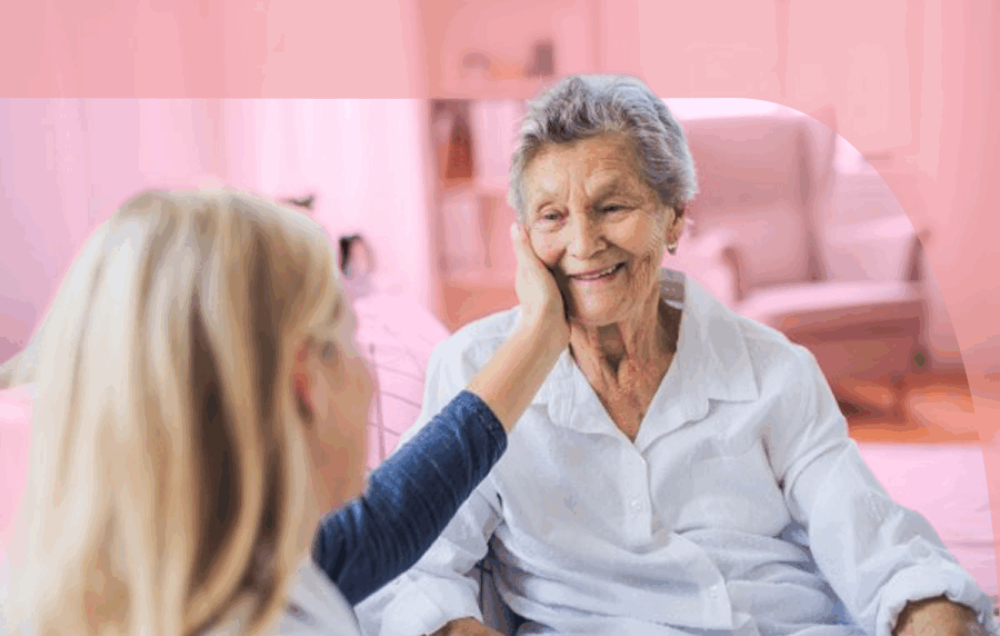 Elderly woman smiling at a younger woman with long blonde hair who is reaching out and touching her cheek