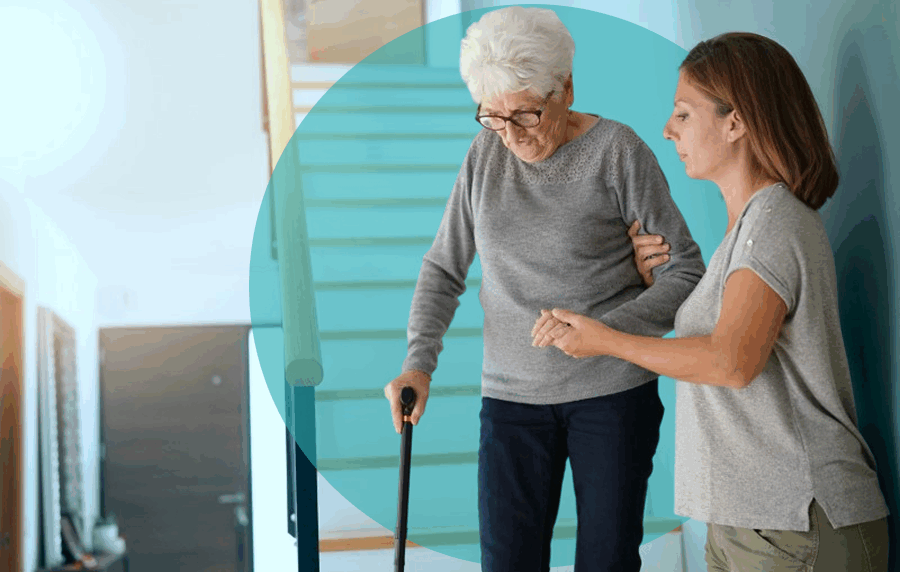 Younger woman helping an elderly woman with a cane walk down the stairs in a home