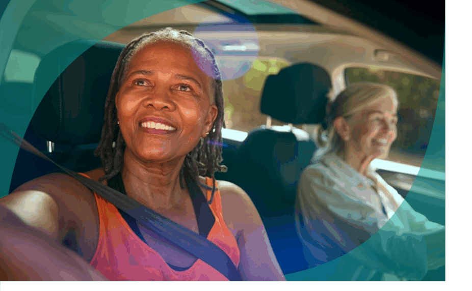 Two senior women in a car, a white woman in the driver's seat in the background and a smiling Black woman looking out the window in the foreground