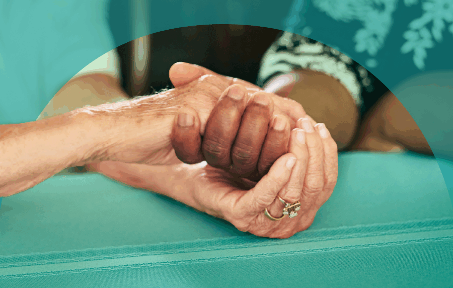 Close-up shot of the hands of an elderly white person holding the hand of an elderly Black person