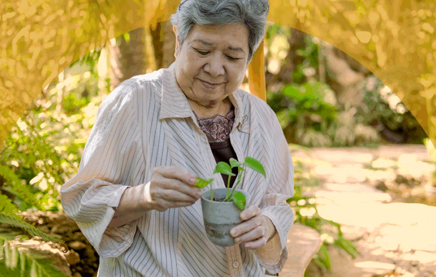 Senior woman with medium skin tone sitting ouside tending to small plant in her hands