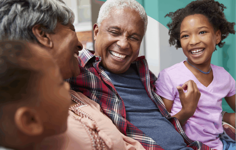 Close-up shot of 4 members of a Black family on a couch smiling at each other - a senior man and woman and two young girls