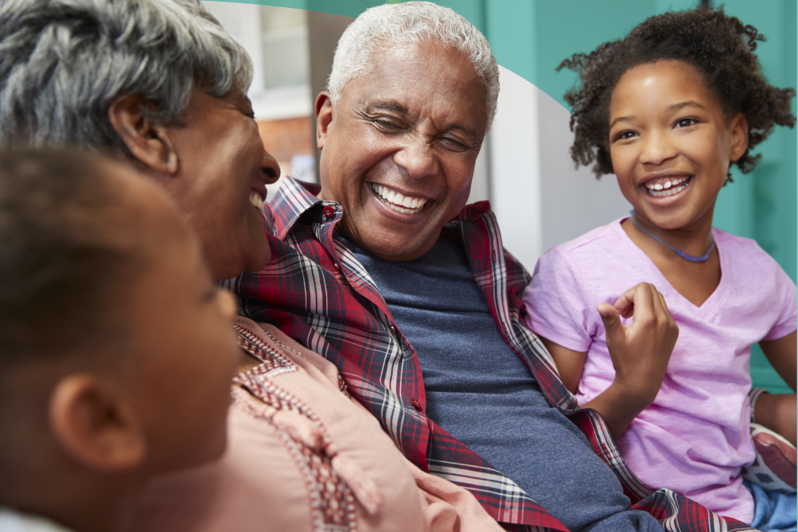 Close-up shot of 4 members of a Black family on a couch smiling at each other - a senior man and woman and two young girls