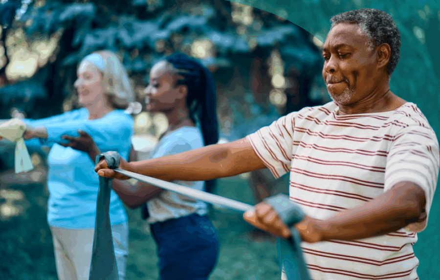 Senior Black man in foreground working out with a resistance band, with a young Black woman instructing a senior white woman in the background