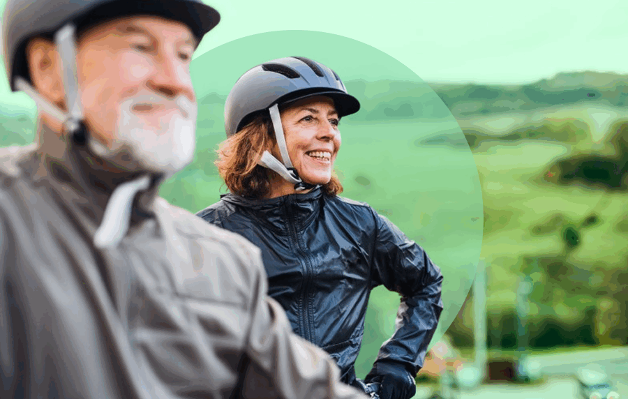 Senior man and woman wearing rain jackets and bike helmets in a lush green setting