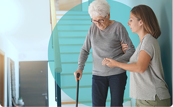Elderly woman using cane assisted by caregiver indoors