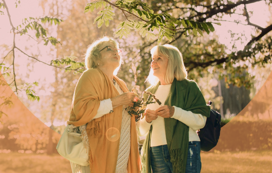 Two white senior women standing outside under a tree canopy and smiling