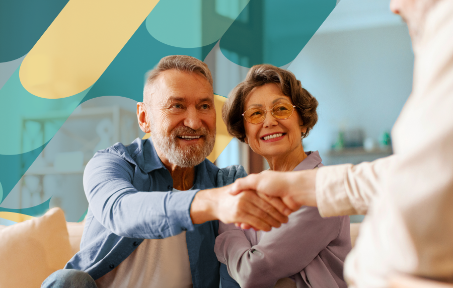 Senior couple sitting down and smiling, the man reaching out to shake the hand of a male agent outside the image frame