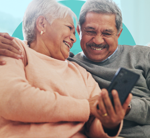Elderly couple smiling and looking at smartphone together on couch.