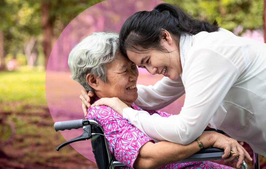 Close-up outdoor photo of an East or Southeast Asian young woman hugging a senior woman who is seated in a wheelchair