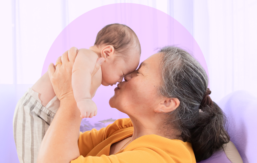 East Asian senior woman nose-to-nose with a newborn baby she is lifting up